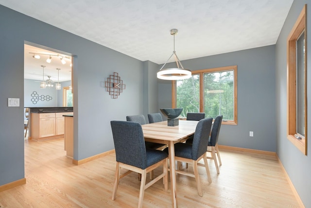 dining area with light wood-type flooring, baseboards, a notable chandelier, and rail lighting