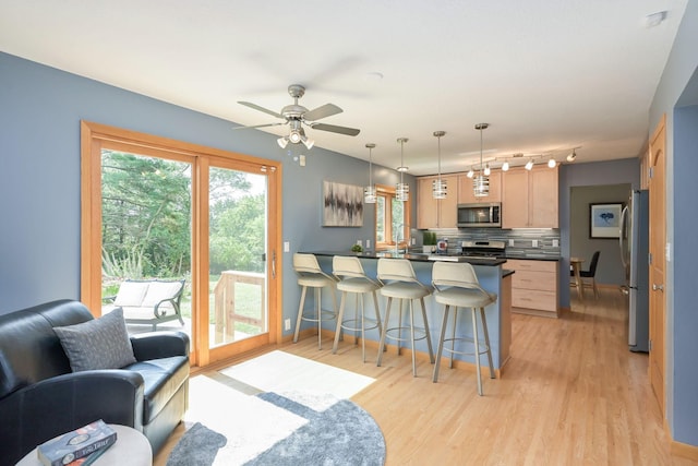 kitchen featuring light wood-type flooring, a kitchen bar, dark countertops, appliances with stainless steel finishes, and decorative backsplash