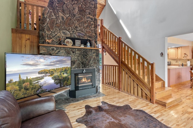 living room with light wood-type flooring, sink, a stone fireplace, and high vaulted ceiling