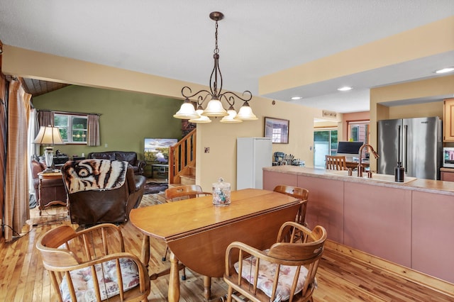 dining room featuring stairs, vaulted ceiling, light wood-type flooring, and a notable chandelier