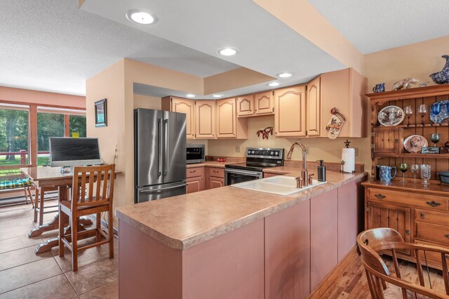 kitchen with sink, appliances with stainless steel finishes, light brown cabinetry, a textured ceiling, and kitchen peninsula