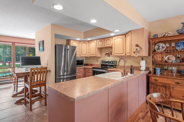 kitchen featuring light brown cabinets, a peninsula, a sink, light countertops, and appliances with stainless steel finishes