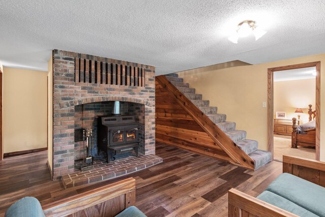 living room featuring a textured ceiling, brick wall, hardwood / wood-style floors, and a wood stove