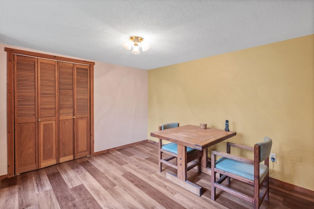 dining area featuring a textured ceiling, light wood finished floors, and baseboards