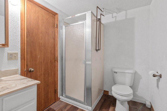 bathroom with toilet, wood finished floors, vanity, baseboards, and a stall shower