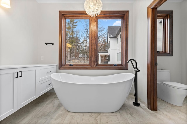 bathroom with a bathtub, a healthy amount of sunlight, toilet, and an inviting chandelier