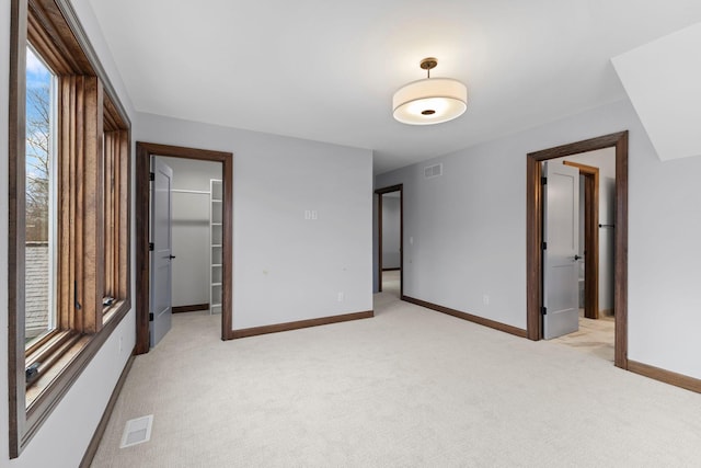 unfurnished bedroom with a walk in closet, a closet, and light colored carpet