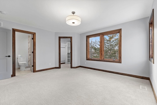 unfurnished bedroom with ensuite bathroom, light colored carpet, a walk in closet, and a closet