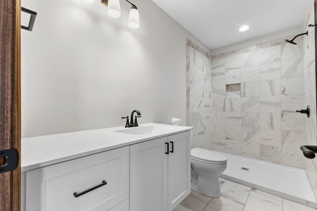 bathroom with a tile shower, vanity, and toilet