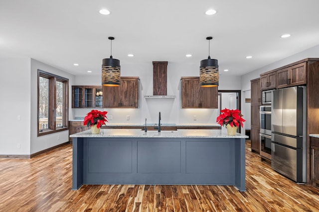 kitchen with stainless steel appliances, light hardwood / wood-style flooring, hanging light fixtures, and wall chimney exhaust hood