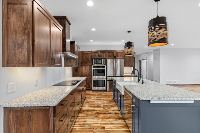 kitchen with appliances with stainless steel finishes, an island with sink, hanging light fixtures, and light hardwood / wood-style floors