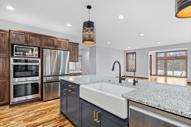 kitchen featuring hanging light fixtures, sink, light hardwood / wood-style flooring, appliances with stainless steel finishes, and light stone counters