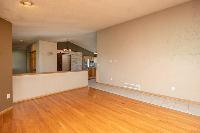 unfurnished living room with vaulted ceiling, light hardwood / wood-style flooring, a textured ceiling, and a chandelier