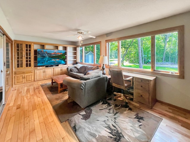 living room with ceiling fan, built in shelves, light hardwood / wood-style floors, and a wealth of natural light