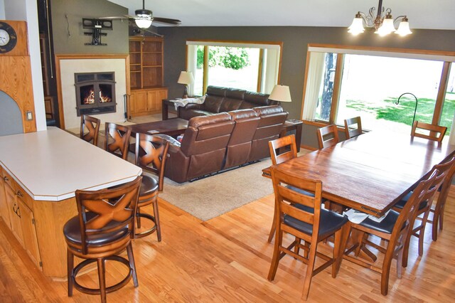 dining space with ceiling fan with notable chandelier, light hardwood / wood-style floors, and lofted ceiling