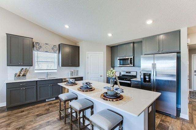 kitchen with appliances with stainless steel finishes, a kitchen breakfast bar, dark hardwood / wood-style flooring, lofted ceiling, and a kitchen island with sink