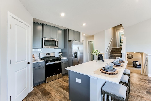 kitchen with dark hardwood / wood-style floors, a kitchen bar, gray cabinetry, backsplash, and appliances with stainless steel finishes