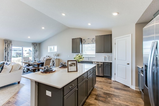 kitchen with a textured ceiling, stainless steel appliances, dark hardwood / wood-style floors, a center island, and vaulted ceiling