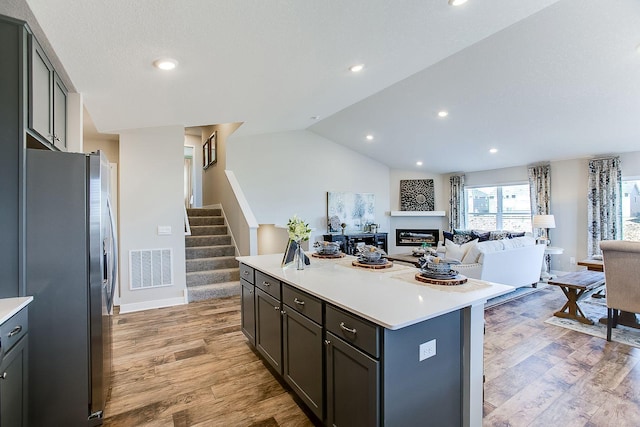 kitchen with stainless steel refrigerator with ice dispenser, light hardwood / wood-style floors, vaulted ceiling, and a kitchen island