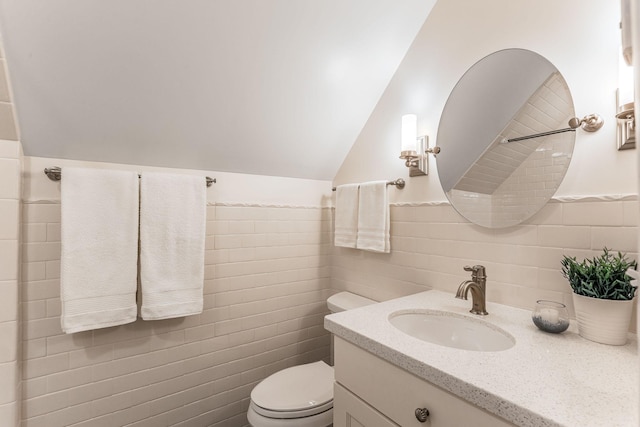 bathroom with lofted ceiling, vanity, toilet, and tile walls