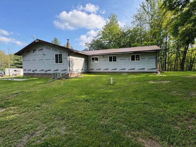 back of house with metal roof, central AC unit, a lawn, and a chimney