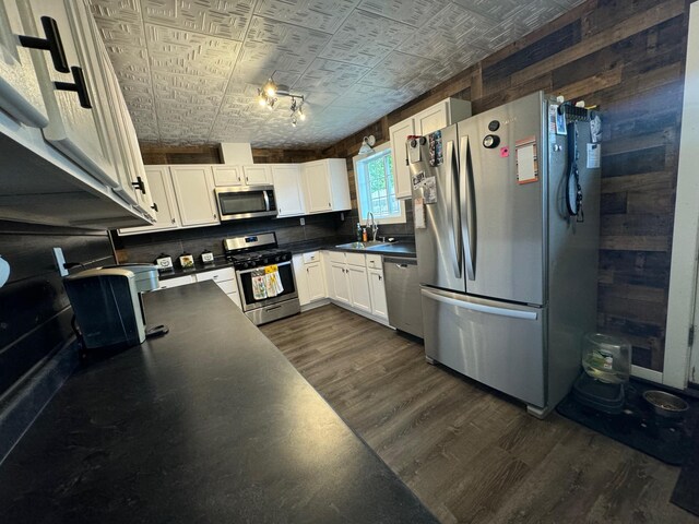 kitchen featuring dark countertops, appliances with stainless steel finishes, dark wood-type flooring, white cabinets, and a sink