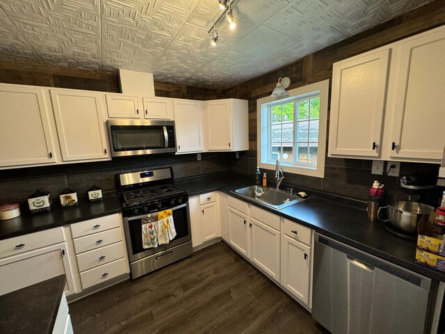 kitchen with appliances with stainless steel finishes, dark countertops, a sink, and white cabinetry