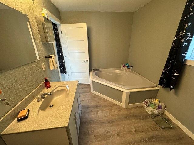 full bathroom with wood finished floors, a garden tub, vanity, and baseboards