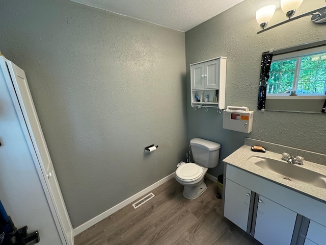 half bathroom featuring a textured wall, wood finished floors, visible vents, vanity, and baseboards