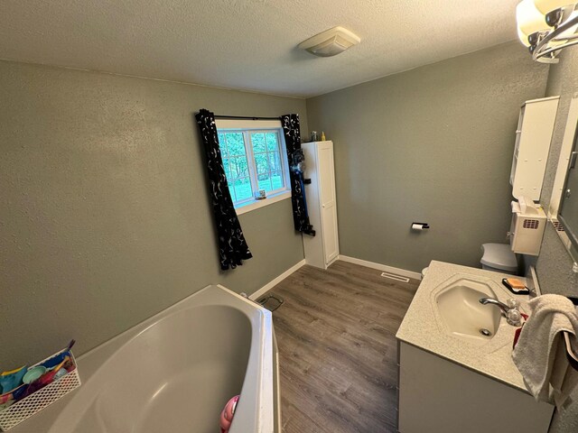 bathroom featuring a garden tub, a textured ceiling, vanity, wood finished floors, and baseboards