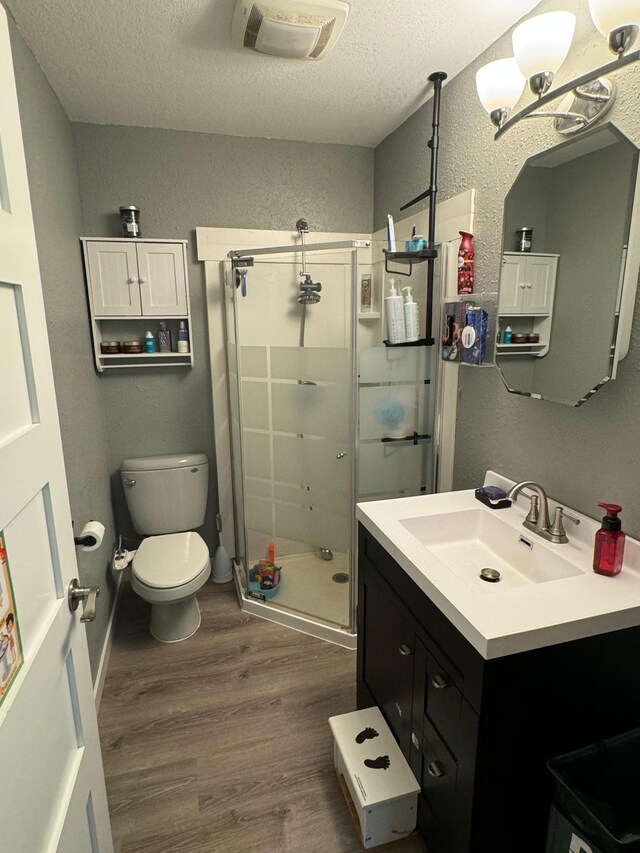 bathroom featuring a textured ceiling, toilet, wood finished floors, vanity, and a stall shower