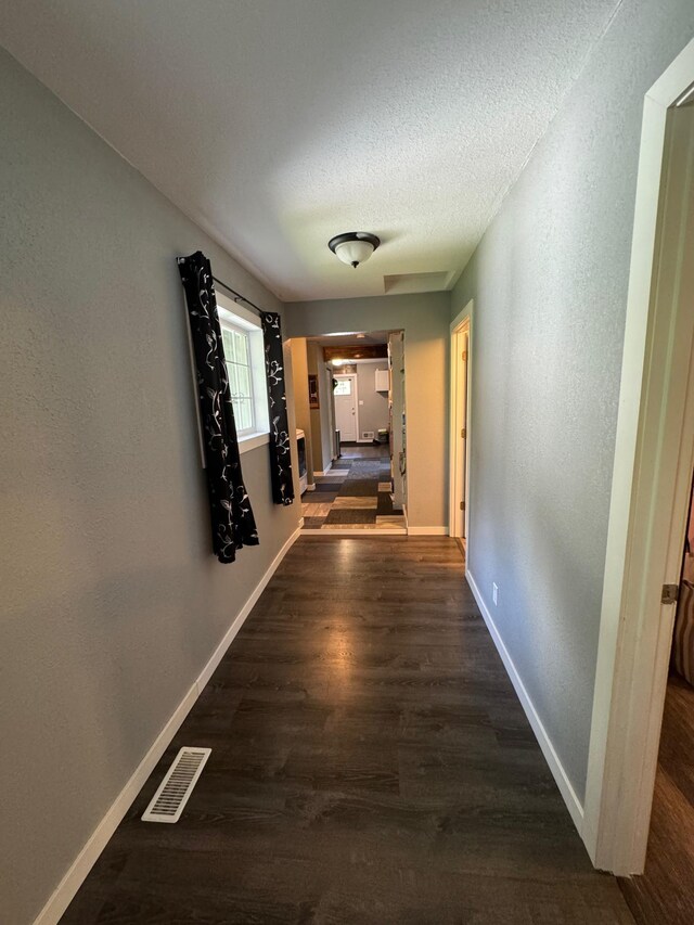 hall with baseboards, visible vents, and dark wood-type flooring