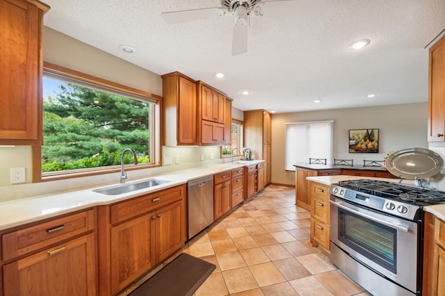 kitchen featuring appliances with stainless steel finishes, brown cabinets, a peninsula, light countertops, and a sink