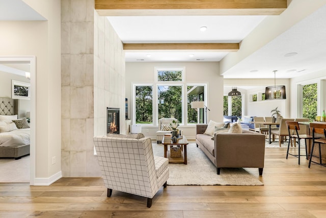 living room with light wood-type flooring, a wealth of natural light, a fireplace, and beamed ceiling