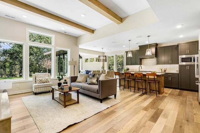 living room with light wood-type flooring, a wealth of natural light, beamed ceiling, and sink