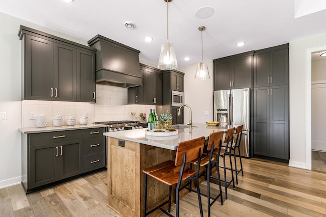 kitchen featuring light wood-type flooring, premium range hood, backsplash, and an island with sink