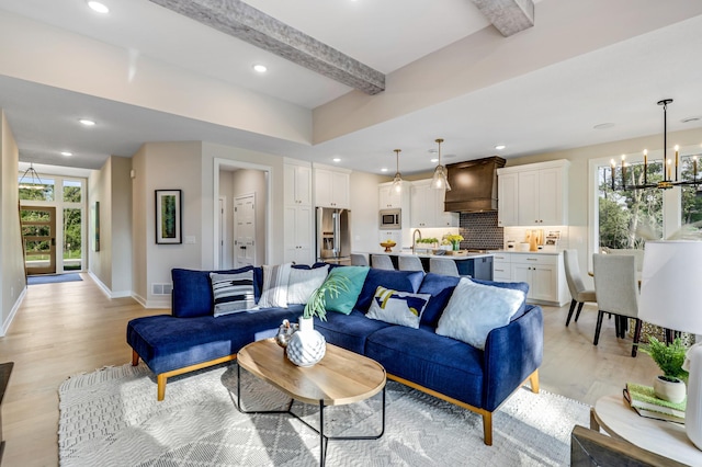 living room featuring beamed ceiling, light hardwood / wood-style flooring, an inviting chandelier, and sink