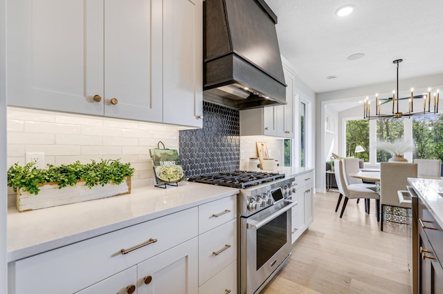 kitchen featuring stainless steel stove, custom range hood, light hardwood / wood-style flooring, pendant lighting, and tasteful backsplash