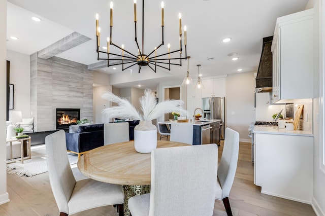 dining room featuring a fireplace, light wood-type flooring, a notable chandelier, sink, and tile walls