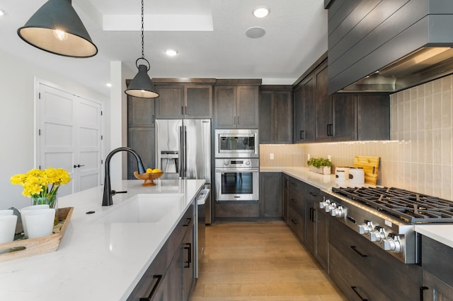 kitchen featuring custom range hood, light hardwood / wood-style flooring, decorative light fixtures, appliances with stainless steel finishes, and tasteful backsplash