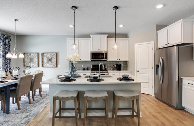 kitchen featuring sink, stainless steel appliances, hanging light fixtures, and an island with sink