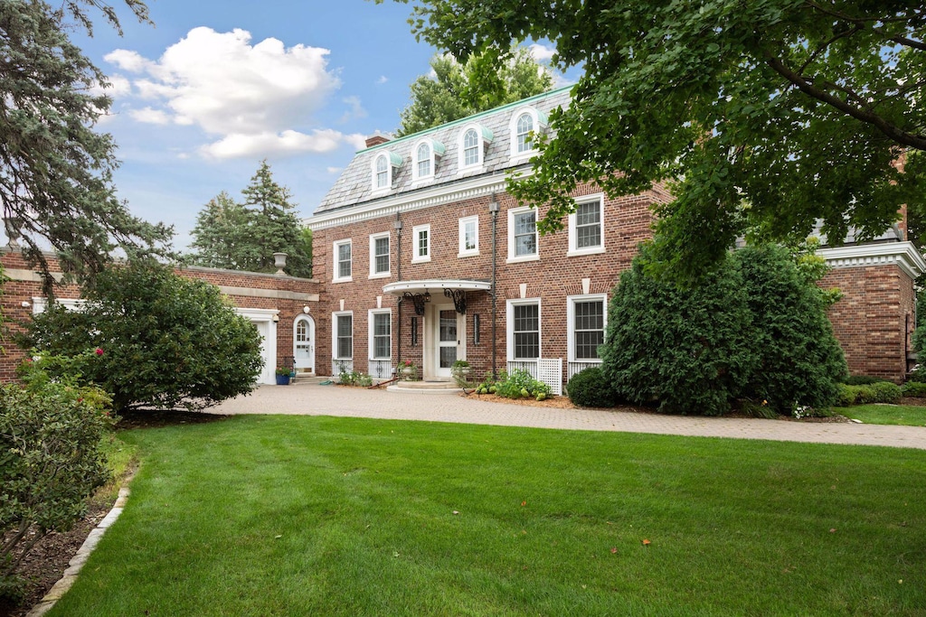 colonial house featuring a high end roof, mansard roof, an attached garage, a front lawn, and brick siding