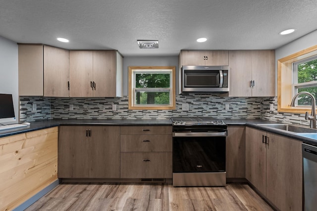 kitchen with decorative backsplash, appliances with stainless steel finishes, a textured ceiling, light wood-type flooring, and sink