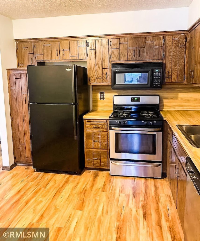 kitchen featuring black appliances, a textured ceiling, light hardwood / wood-style flooring, and sink