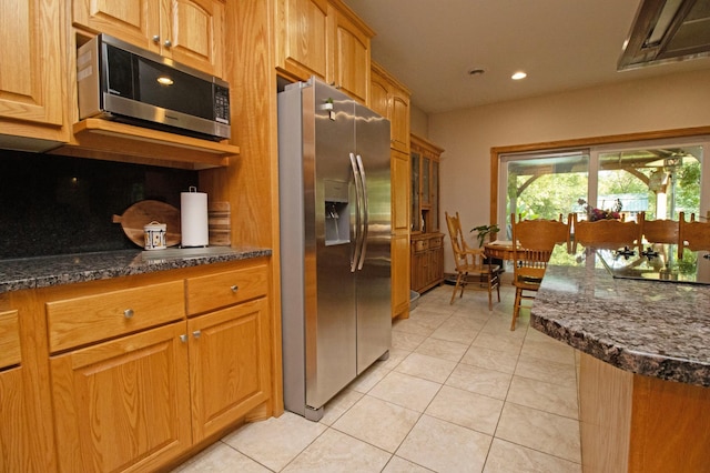 kitchen with light tile patterned flooring, recessed lighting, brown cabinets, dark stone countertops, and appliances with stainless steel finishes