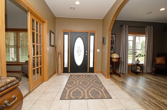 entrance foyer with a healthy amount of sunlight, arched walkways, light tile patterned floors, and baseboards
