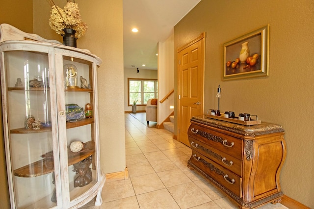 hallway featuring baseboards, a textured wall, light tile patterned floors, and stairway