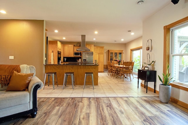 kitchen featuring dark countertops, appliances with stainless steel finishes, a peninsula, island exhaust hood, and light wood-type flooring