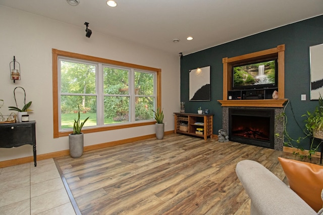 living room featuring baseboards, recessed lighting, wood finished floors, and a warm lit fireplace