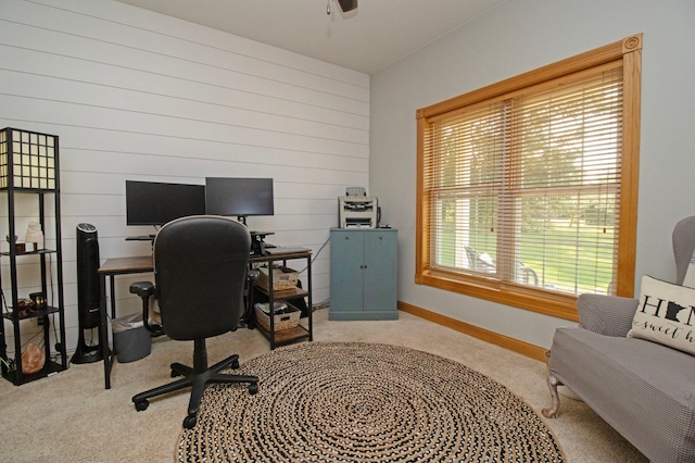 office area featuring carpet floors, wood walls, baseboards, and ceiling fan